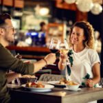 young-happy-couple-celebrating-toasting-with-wineglasses-while-eating-restaurant