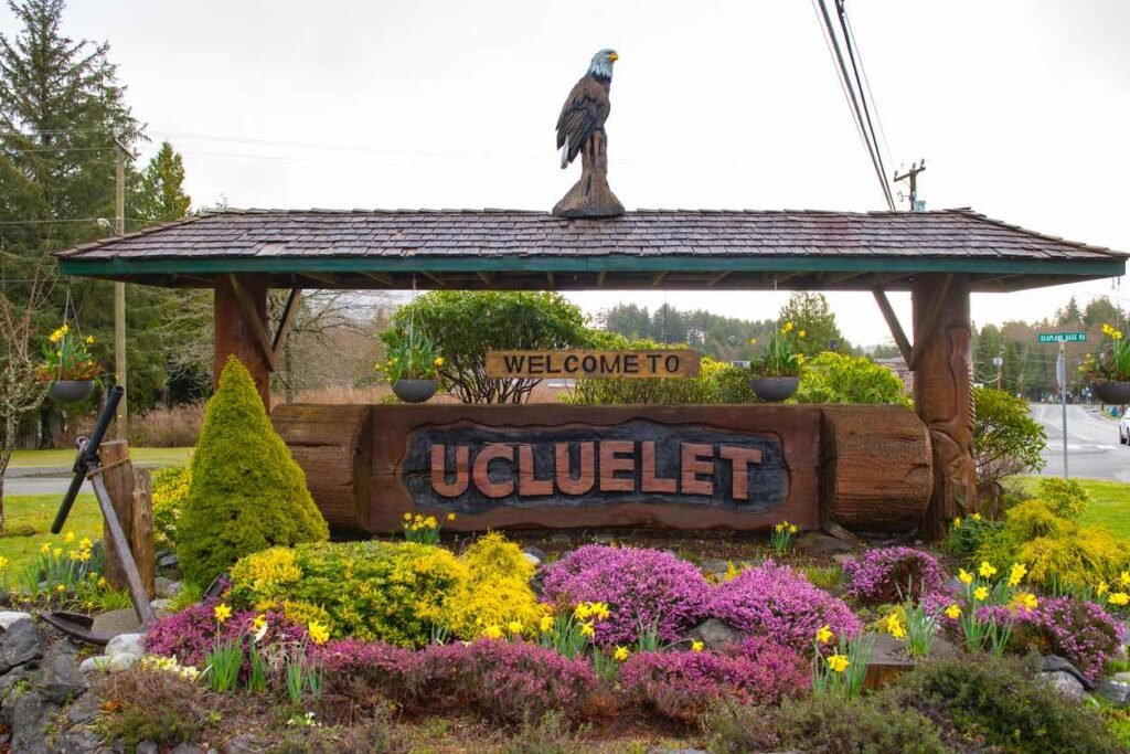 Welcome to Ucluelet wooden sign surrounded by blooming flowers in spring, marking the entrance to the coastal town on Vancouver Island.