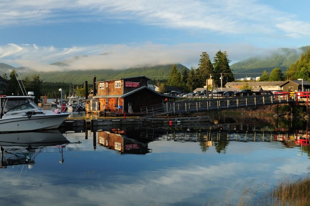 Scenic view of Ucluelet harbor at sunset with fishing boats, wooden buildings, and calm water reflecting the sky and mountains.