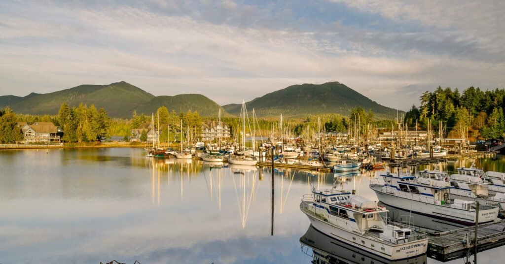 Peaceful marina filled with boats and yachts reflecting in calm water, backed by forested mountains under a partly cloudy sky at Ucluelet
