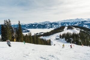 Skiers descending snowy slopes at Sasquatch Mountain with ski lifts and snow-covered evergreen forests, overlooking a frozen lake and dramatic mountain peaks in British Columbia