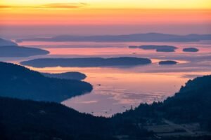 Aerial view of the Southern Gulf Islands in British Columbia at sunset during fall, with golden light reflecting on the ocean and forested islands.