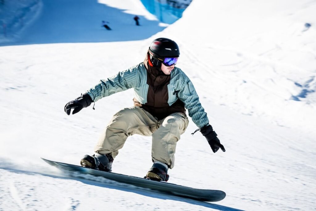 Snowboarder in teal jacket and goggles carving down a pristine white slope with mountain ridges in the background at a British Columbia ski resort
