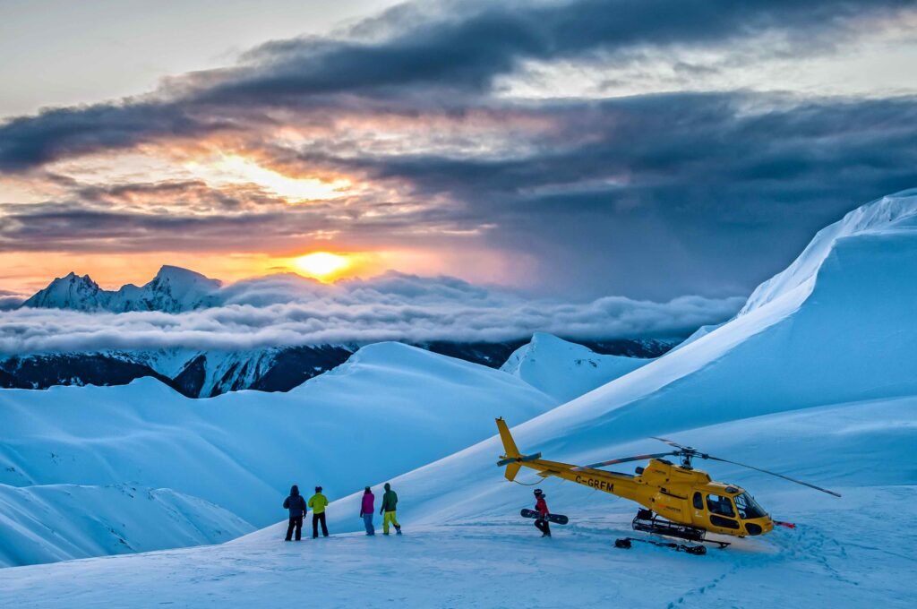 Skiers preparing for a helicopter drop at sunset in Northern British Columbia's Coast Mountains with Last Frontier Heliskiing, showing deep powder snow and dramatic mountain peaks