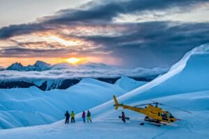 Skiing Northern British Columbia. Skiers preparing for a helicopter drop at sunset in Northern British Columbia's Coast Mountains with Last Frontier Heliskiing, showing deep powder snow and dramatic mountain peaks