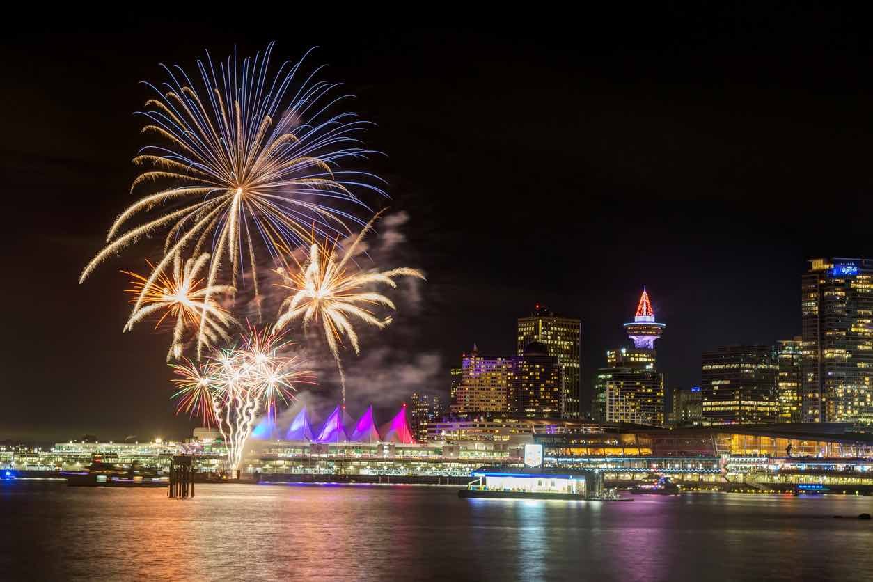  New Year's Eve in Vancouver: Colorful fireworks exploding over Vancouver's illuminated waterfront on New Year's Eve, with Canada Place's iconic white sails and city skyline reflecting in the harbor waters.