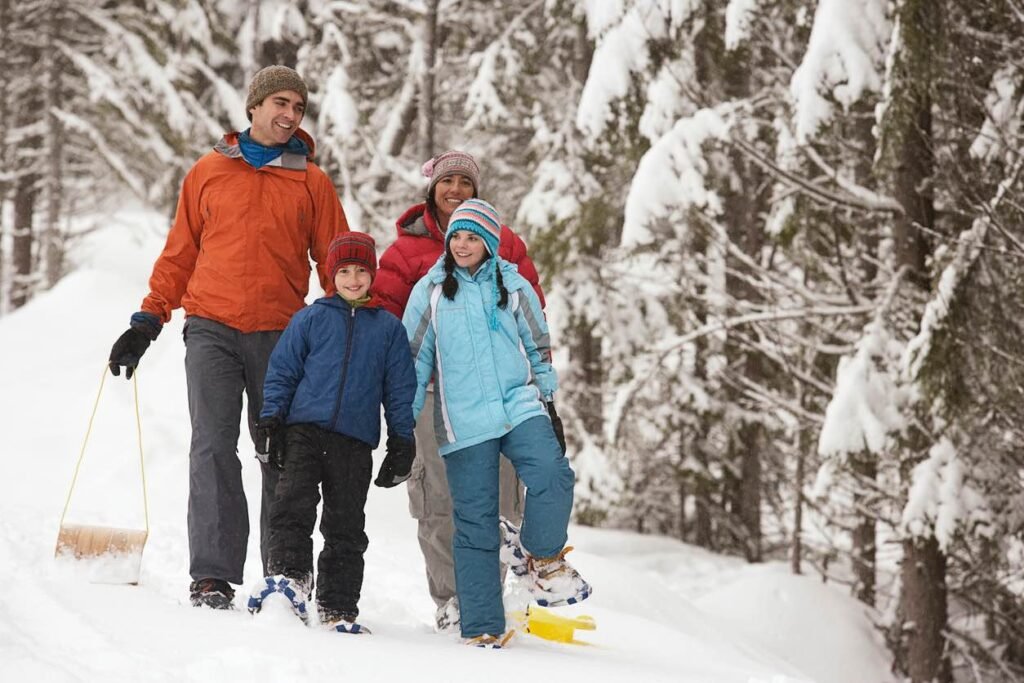 A family walking through a snow-covered forest at Grouse Mountain, with adults and children dressed in winter clothing and pulling a sled, illustrating a family-friendly alpine experience close to Vancouver.