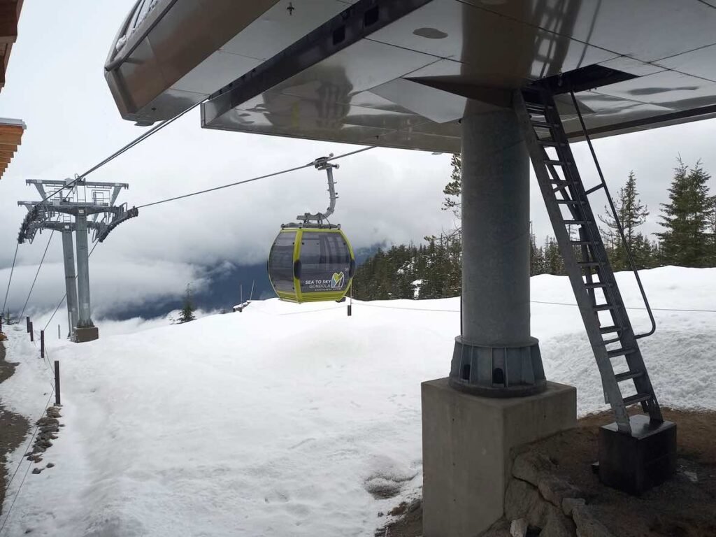 Yellow and grey Sea-to-Sky Gondola cable car approaching station through misty winter weather with snow-covered ground and evergreen trees